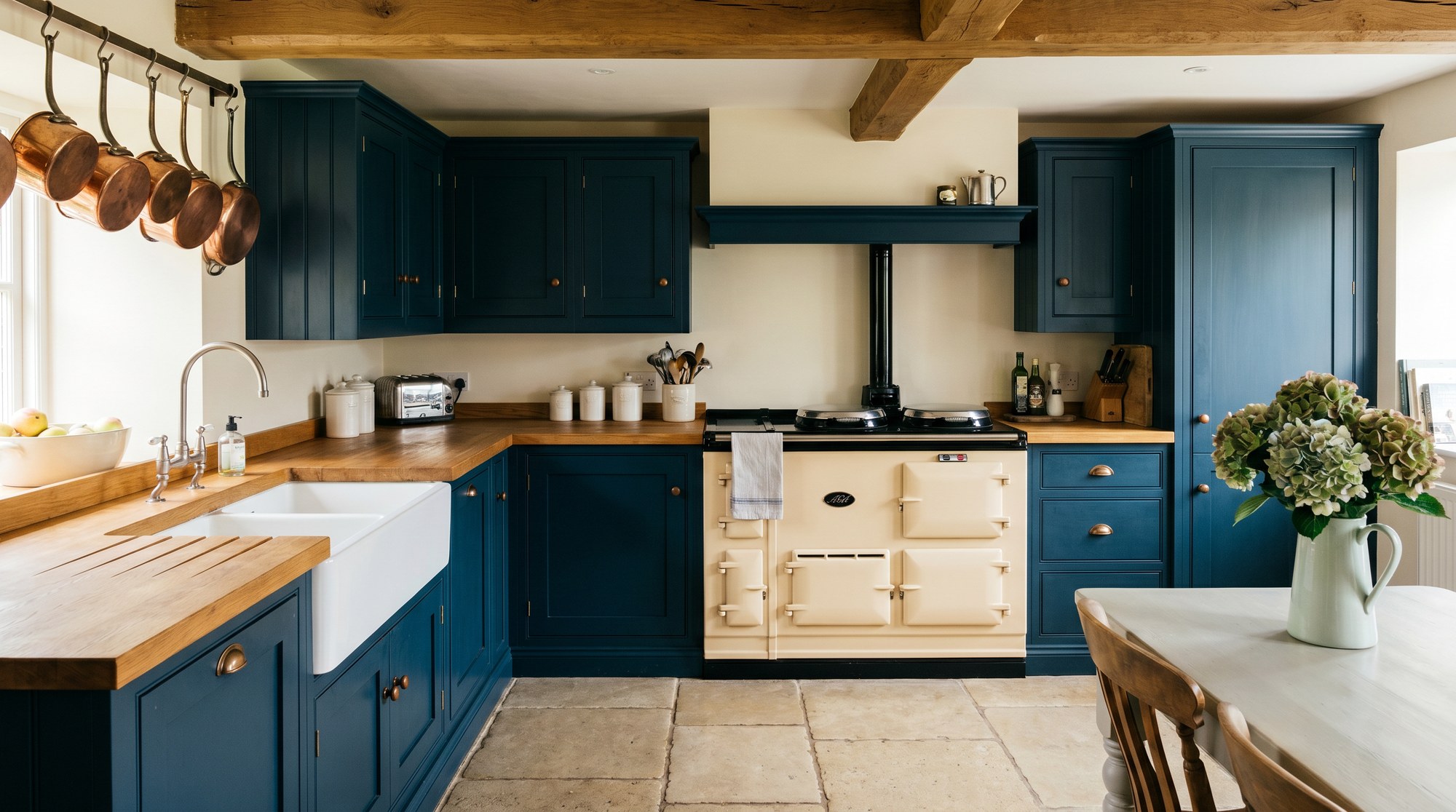 Reeve & Co Farmhouse kitchen hero — Hague Blue V-groove Shaker, cream AGA, Belfast sink, oak beams, limestone flagstones
