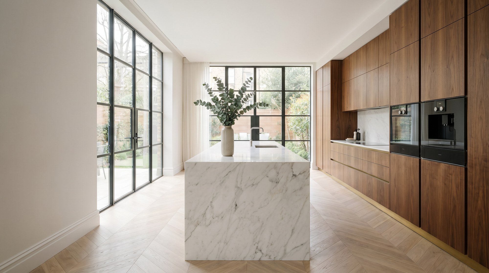 Reeve & Co Kensington kitchen hero — book-matched walnut handle-less cabinetry, Calacatta marble waterfall island, crittall windows